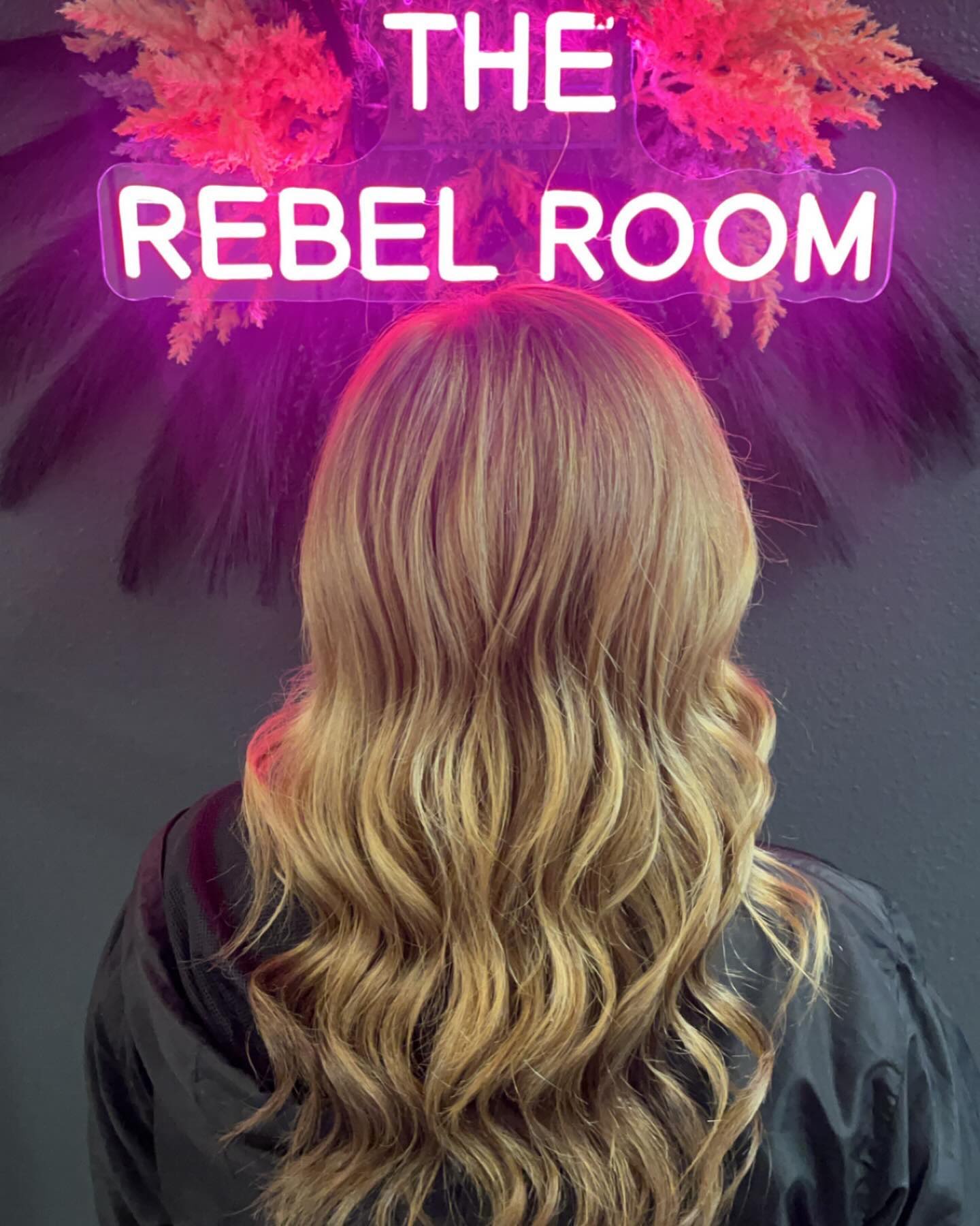 A finished blonde blowout under the neon THE REBEL ROOM sign in Stephanie's suite